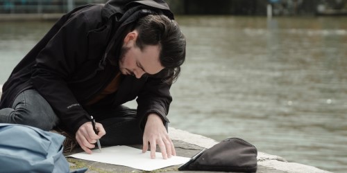 Cai Burton drawing his Cabot Conversations artwork by Bristol Harbourside